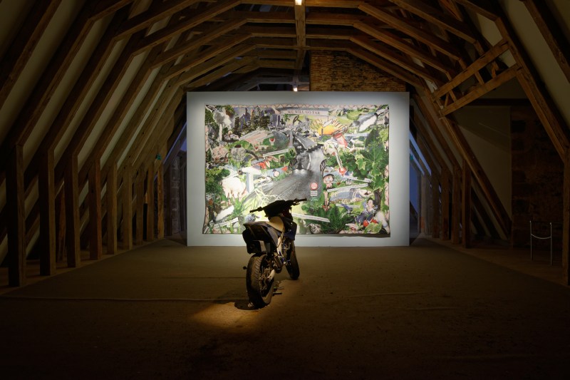 Laure Prouvost, The Smoking Image, 2015, tapisserie, vidéo (8.40 min), motos, machines à fumée, terre, moquette, œufs, smartphones, plumes.  Vue de l’exposition MDAC Rochechouart.  Courtesy de l’artiste, de MOT international (Londres, Bruxelles) et de la Galerie Nathalie Obadia (Paris, Bruxelles). Photo Aurélien Mole