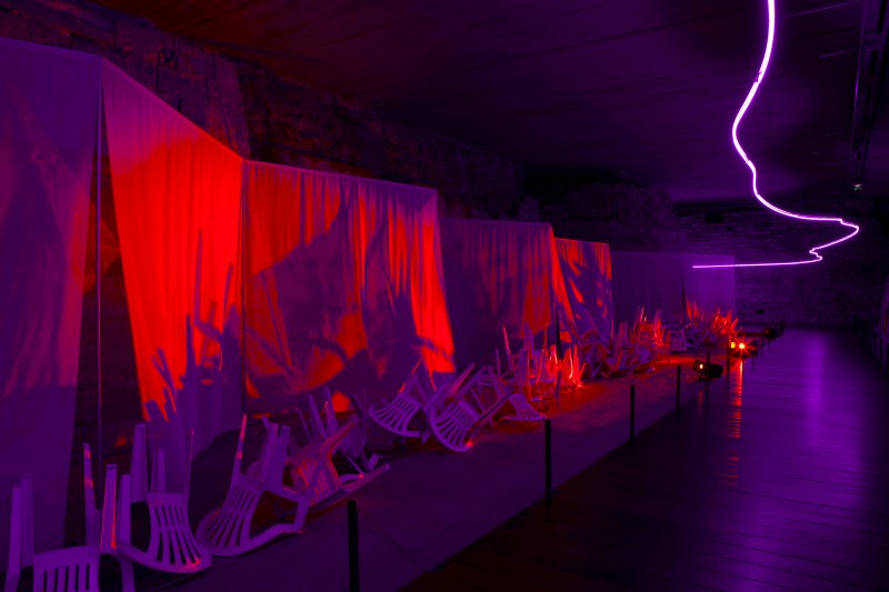 Claude Lévêque Sous le plus grand chapiteau du monde (partie 2), 2015  Dispositif in situ, fossés du Louvre médiéval, Musée du Louvre, Paris  Néon mauve, dessin Romaric Etienne Paravents de voilages, chaises de jardin, projecteurs à découpe, ventilateurs. Diffusion sonore : accords de guitare. Conception sonore en collaboration avec Gerome Nox Photo Julie Joubert © ADAGP Claude Lévêque. Courtesy the artist and kamel mennour, Paris.  
